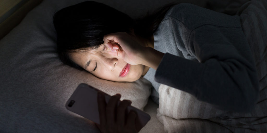 Woman rubbing her eyes while using her phone at night