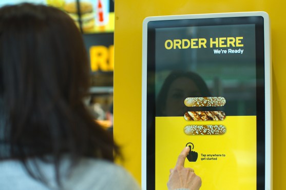 Person ordering fast food from a large wall-mounted touchscreen